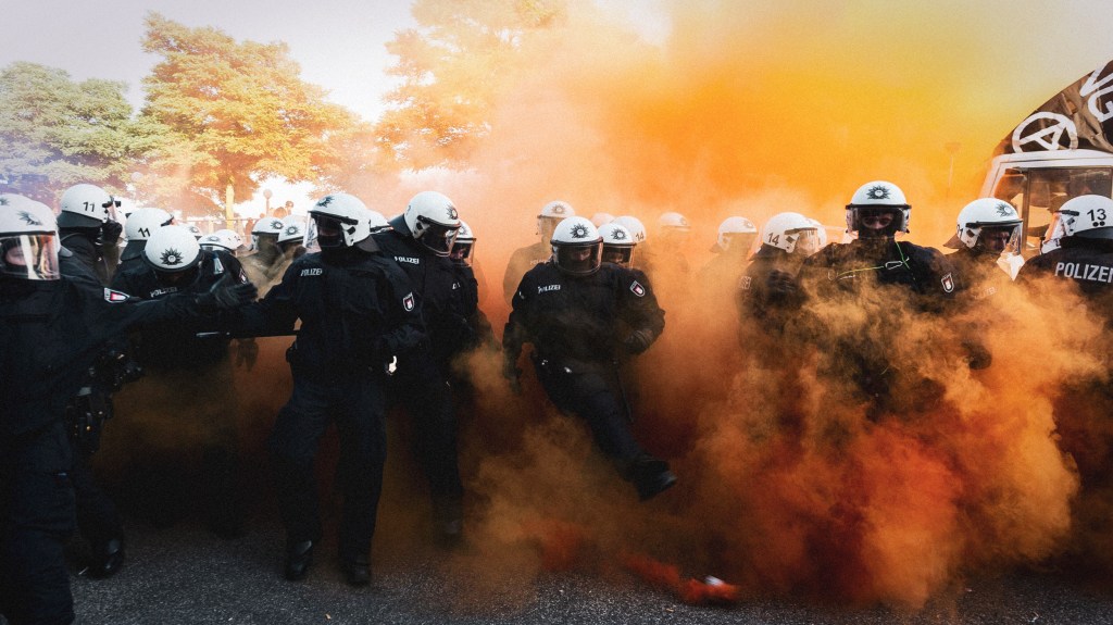 Die Polizei inmitten des orangefarbenen Rauchs einer Rauchbombe. Wir haben mit dem Kriminologen Rafael Behr darüber geredet, wie man die Polizei reformieren sollte