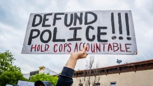 Tangan demonstran mengangkat spanduk bertuliskan "Defund the Police"