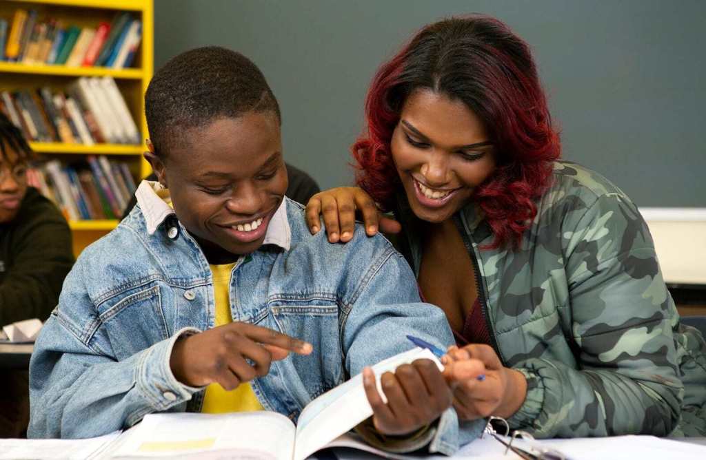 A transfeminine student and masculine student laughing together in class.