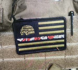 A patch sewn onto the tactical vest worn by Air Force Staff Sergeant Steve Carillo shows a flag with an igloo and a ribbon of Hawaiian shirt print, a symbol used by Boogloo Bois using homophones "Blue Igloo" and "Big Luau."