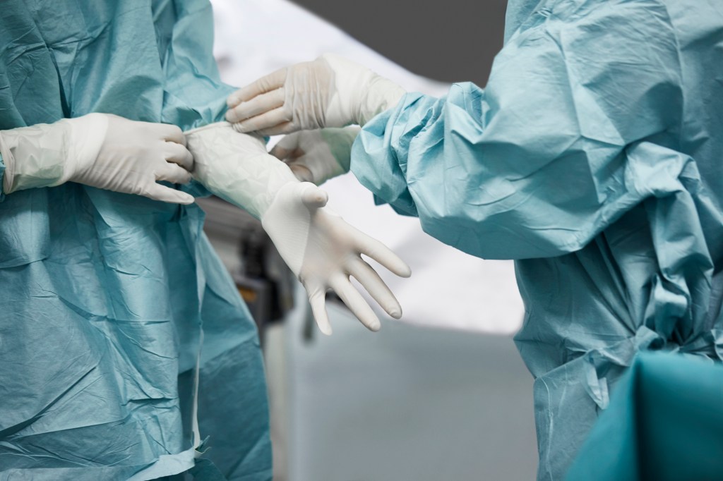 Midsection of doctor helping surgeon put on surgical glove. They are standing in emergency room.