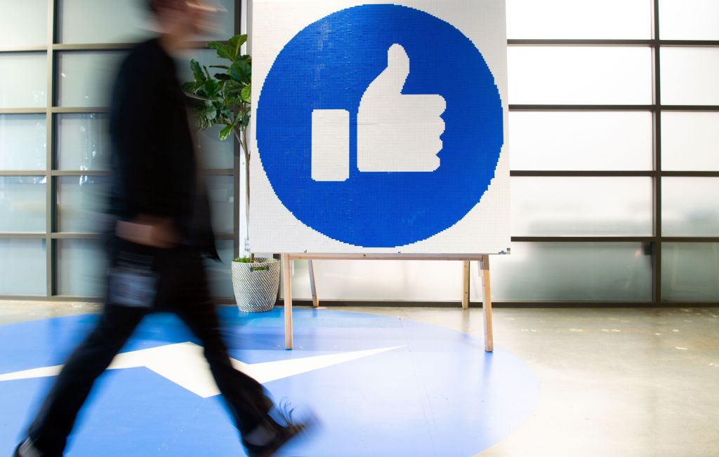 A Facebook employee walks by a sign displaying the "like" sign at Facebook's corporate headquarters campus in Menlo Park, California, on October 23, 2019.