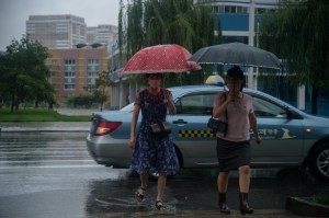 Dua pejalan kaki berpayung menyeberang jalan Mirae Scientists di Pyongyang pada 5 Agustus 2020. Foto oleh Kim Won Jin/AFP