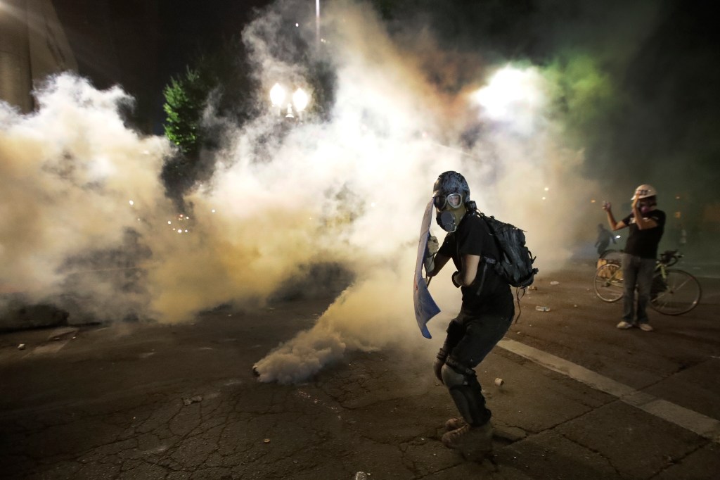 A demonstrator tries to shield himself from tear gas deployed by federal agents during a Black Lives Matter protest at the Mark O. Hatfield United States Courthouse Wednesday, July 29, 2020, in Portland, Ore. (AP Photo/Marcio Jose Sanchez)