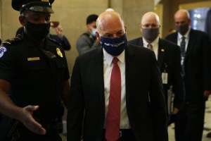 Postmaster General Louis DeJoy walks through the U.S. Capitol wearing a USPS face mask.