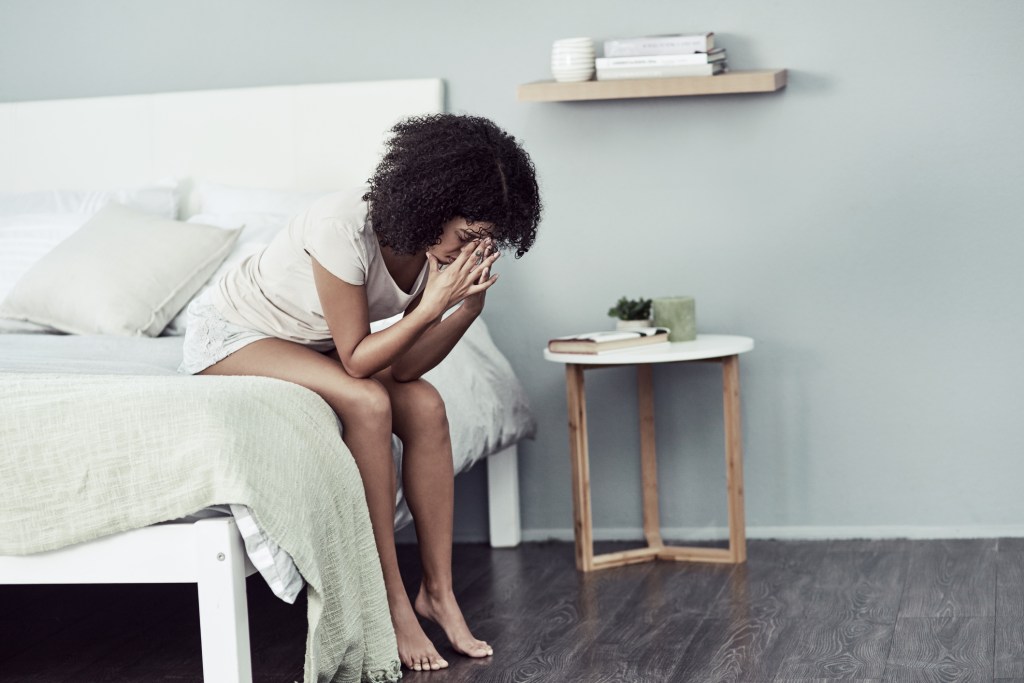 A woman sits on the end of a bed with her head in her hands