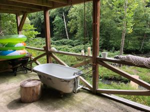 An outdoor tub and some pool floaties sit on a deck of a house next to a river in a forest.