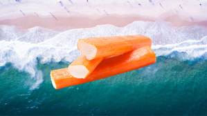 Three orange crab sticks staked on top of each other. Background: view from above of aqua blue ocean waves crashing on a white sand beach.