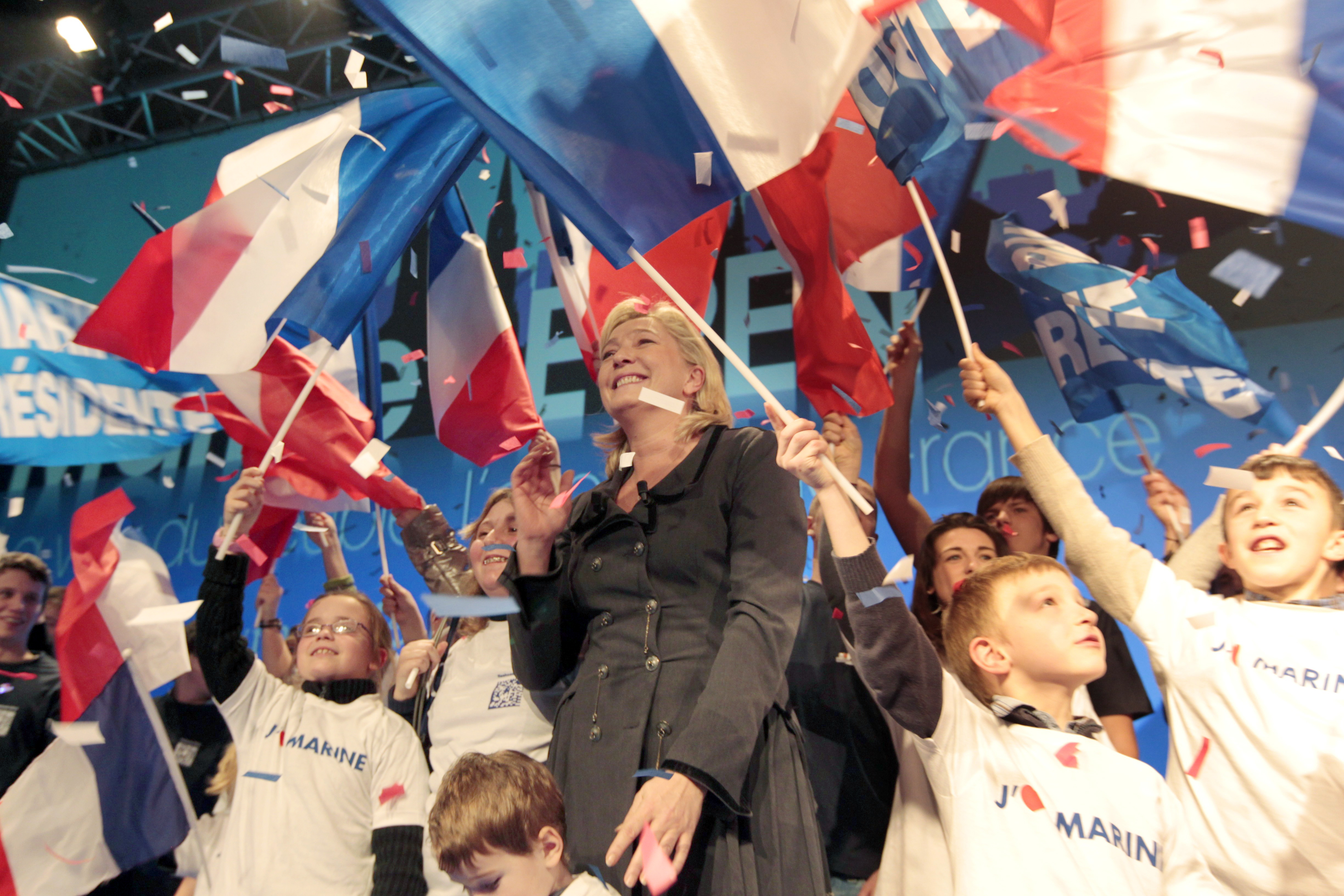 Marine Le Pen surrounded by French youth waving flags.