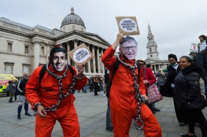 Protesters in red jumpsuits with chains around  their necks wear masks of British Exchequer Rishi Sunak and Bill Gates in Trafalgar Square, London.