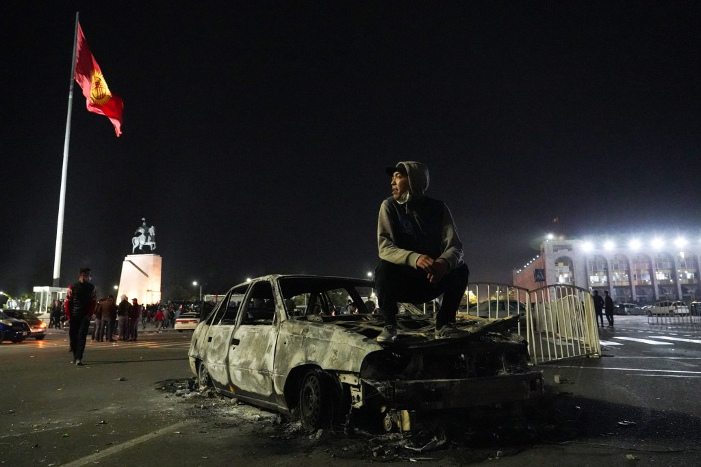 A man sits on a burned out vehicle in central Bishkek after a protest against the results of the 2020 Kyrgyz parliamentary election.​