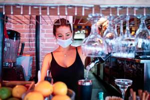 Bartender pours drink while wearing mask.