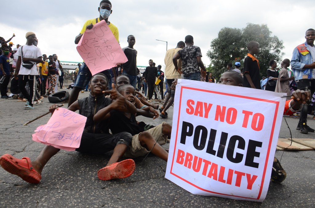 Protestors sit with a sign in Nigeria that says "Say No To Police Brutality"