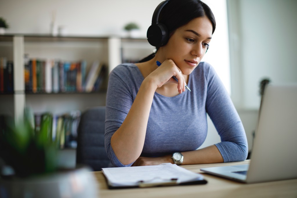 ​A young woman wearing headphones working from home