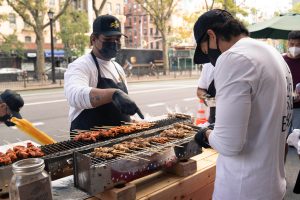 a street food vendor from so sarap grilling filipino barbecue on the sidewalk outside kabisera coffee shop in new york city