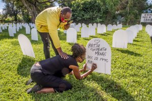 Rachel Moore honors her mother, Patsy Gilreath Moore, by writing her mother's name on a tombstone as Leroy Lee reaches out to comfort her at at Simonhoff Park in the Liberty City neighborhood of Miami, Wednesday, Oct. 14, 2020 (Al Diaz/Miami Herald via AP