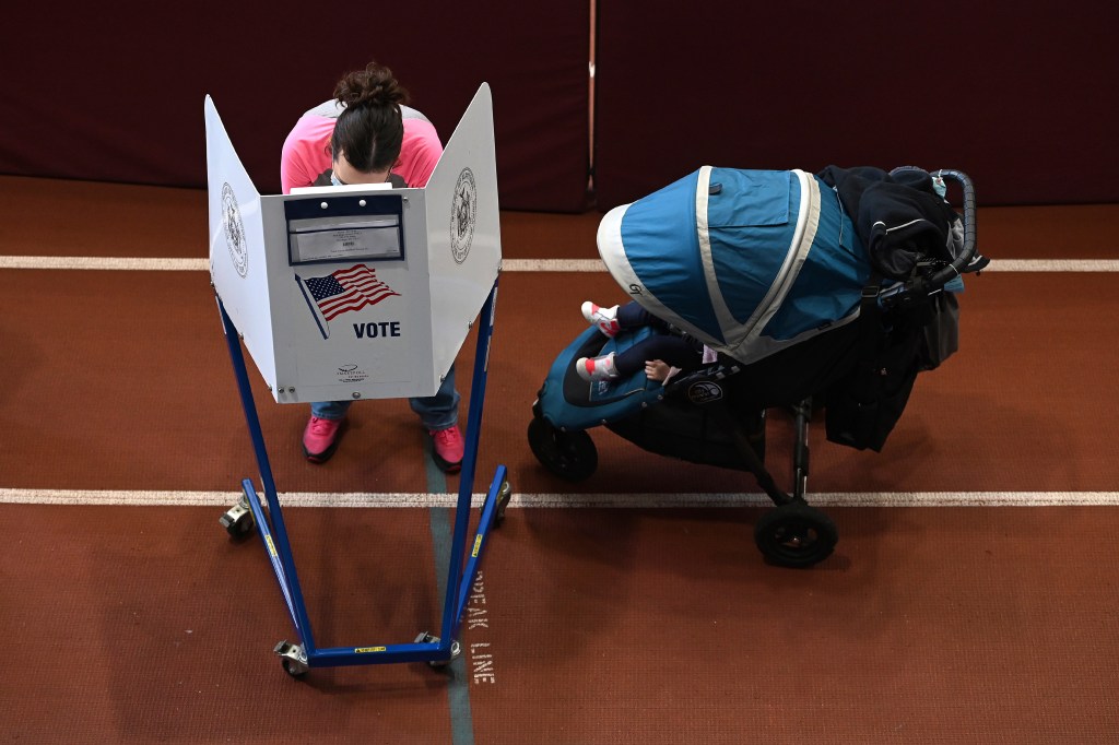 A child sits in stroller parked next to her parent as they as they fill out their ballots behind voter privacy booths inside the Park Slope Armory YMCA on the fourth day of early voting, in the Brooklyn borough of New York City, NY, October 27, 2020.