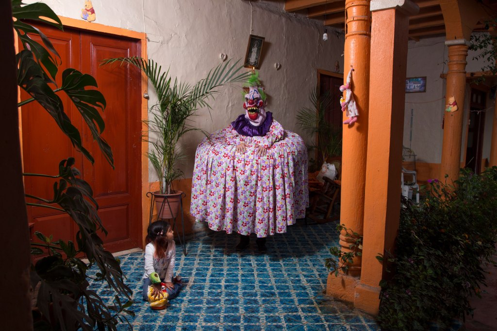 diego moreno's photography "the last breath" showing a child staring at a scary clown in a flower-printed dress