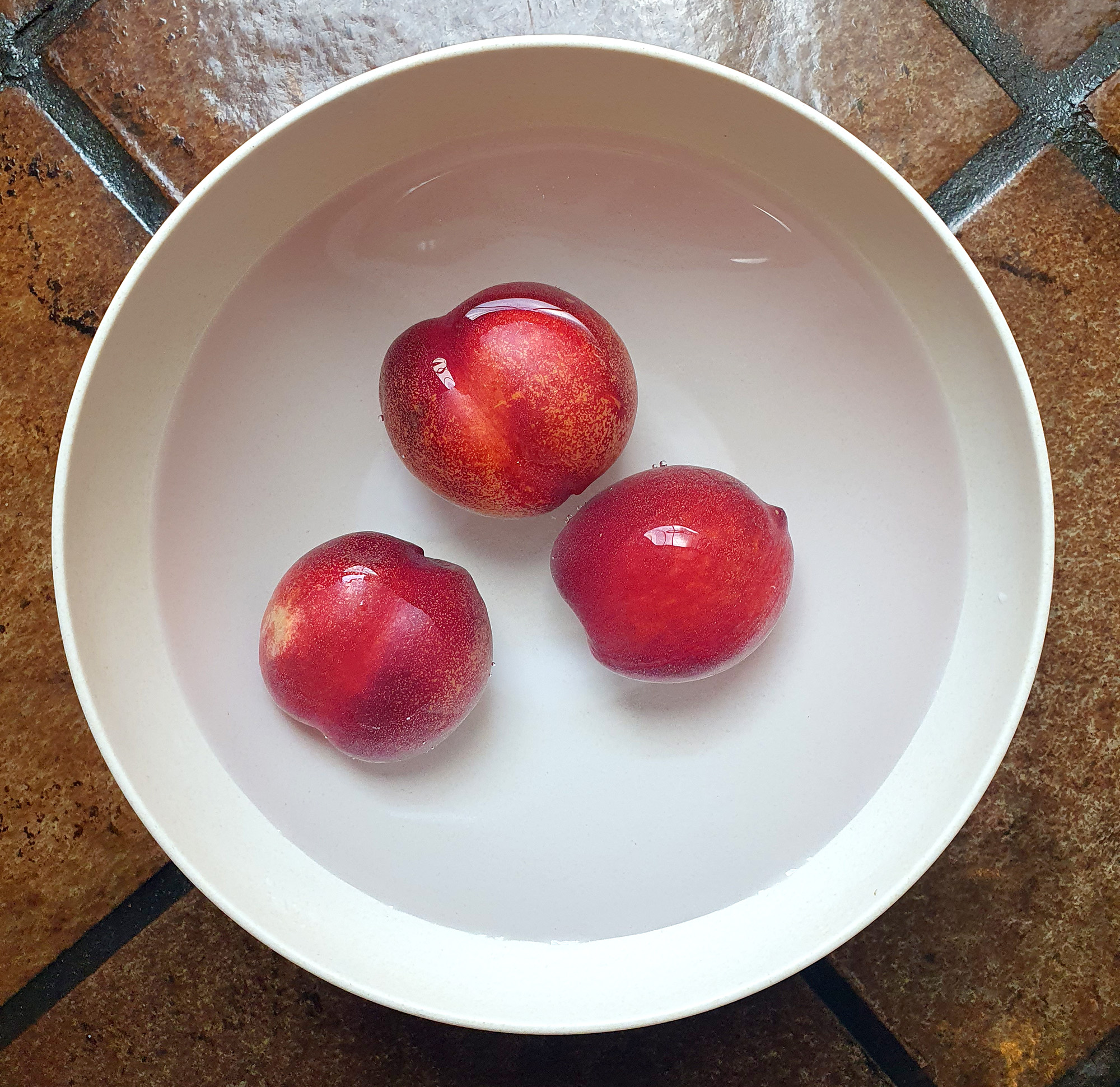 Tiga buah nektarin direndam dalam larutan baking soda. Foto oleh penulis.