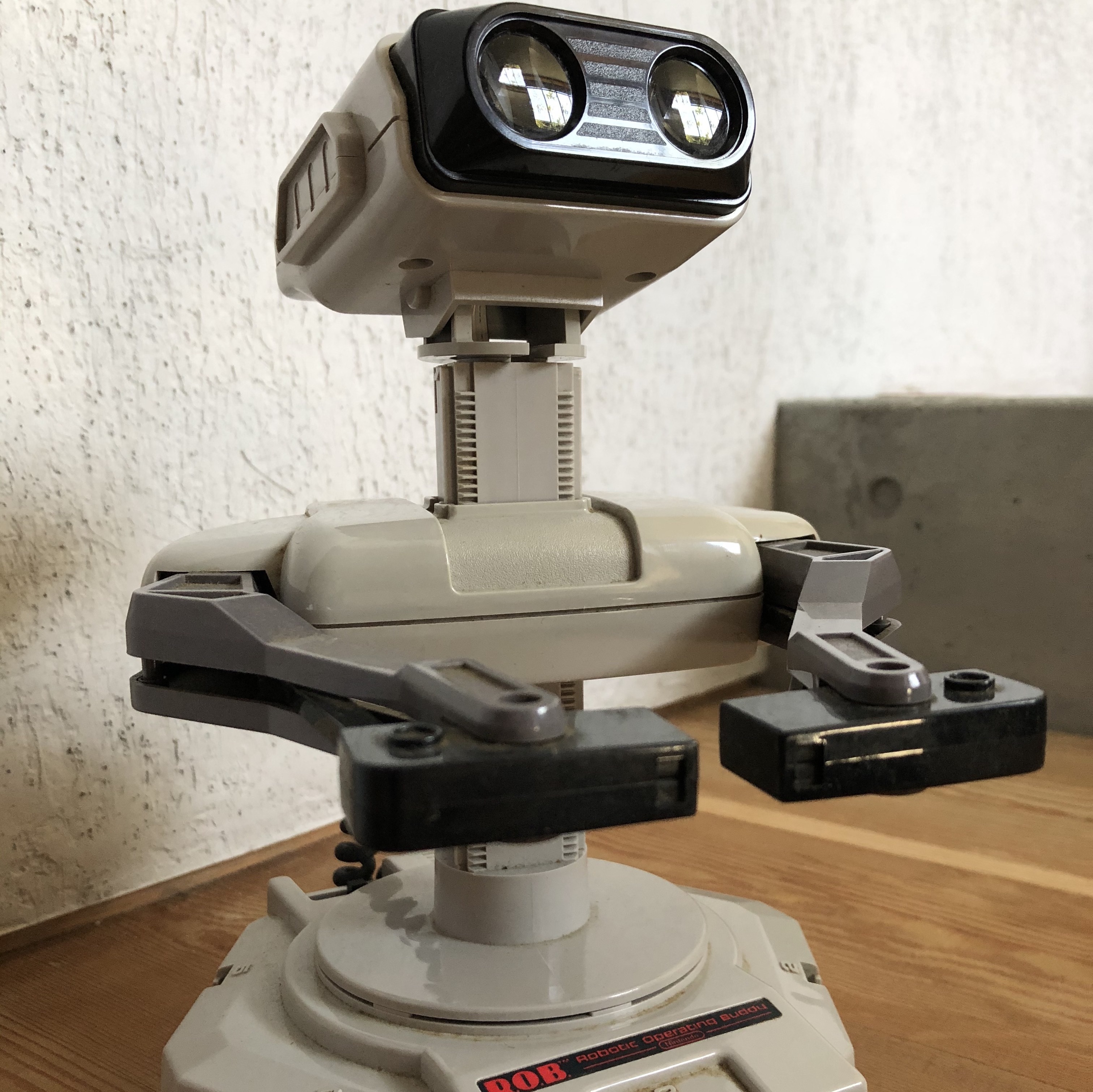 A simple robot with two large Wall-E style eyes atop a head attached to a chunky plastic body via a thick adjustable neck. The legend R.O.B. is etched on its base.