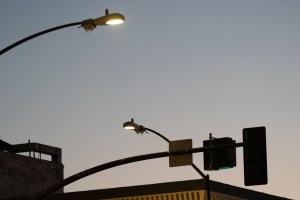 Streetlights equipped with surveillance cameras rise above the streets of San Diego during sunset.