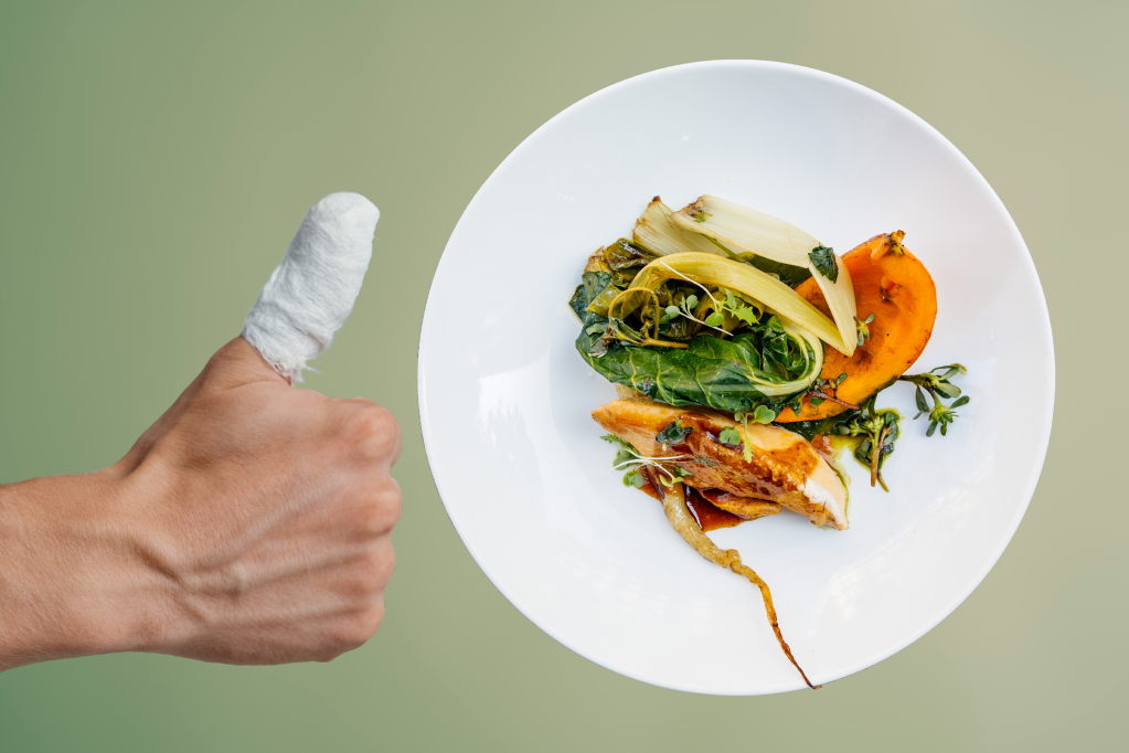 Hand with a bandage giving the thumbs up in front of a fancy plate.