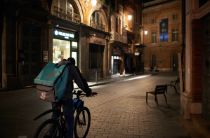 A cyclist with a Deliveroo backpack makes their way down a cobblestone street in Paris at night.