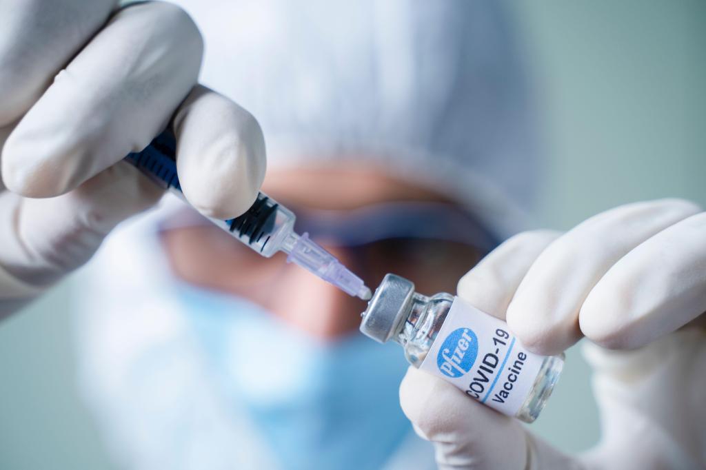 Doctor holding Pfizer BioNtech vaccine and syringe to protect against coronavirus COVID-19 disease.​