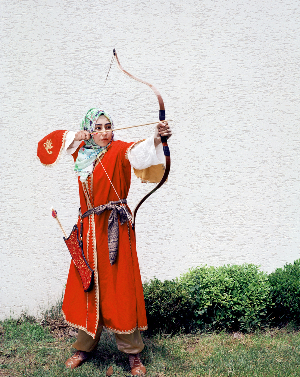 Mathias Depardon - Transanatolia. Woman wearing traditional red garments and pulling the string of an arch