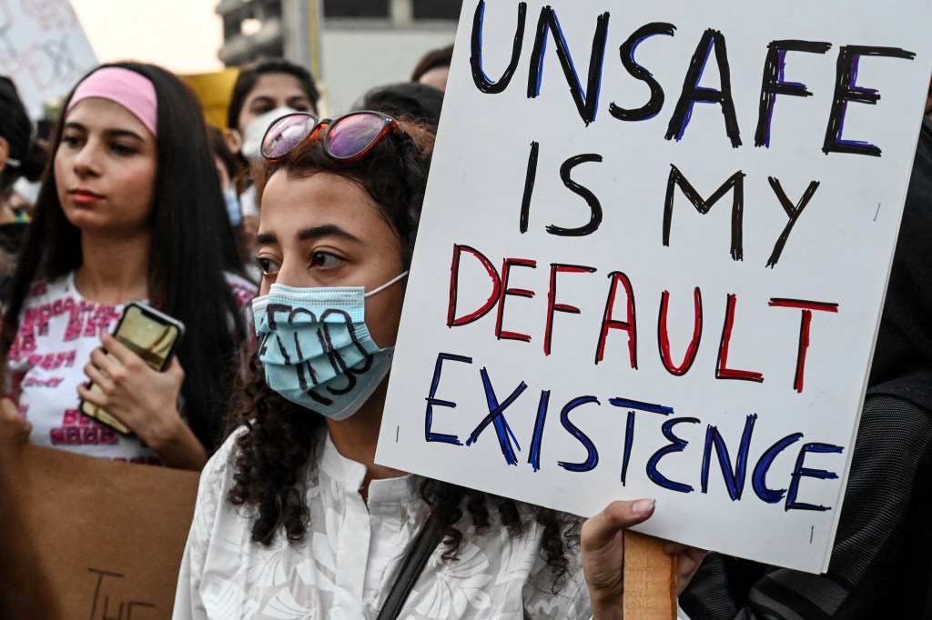 Perempuan mengangkat poster bertuliskan "unsafe is my default existence"