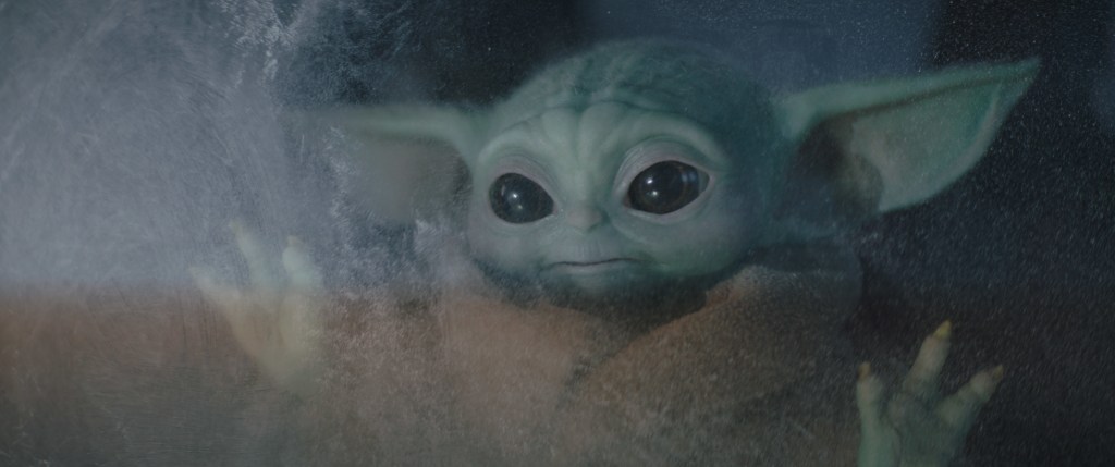 Baby Yoda staring longingly through a window.