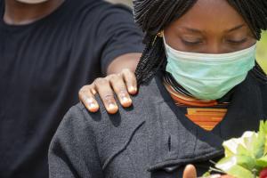 Perempuan kulit Hitam mengenakan masker dan menunjukkan raut wajah sedih