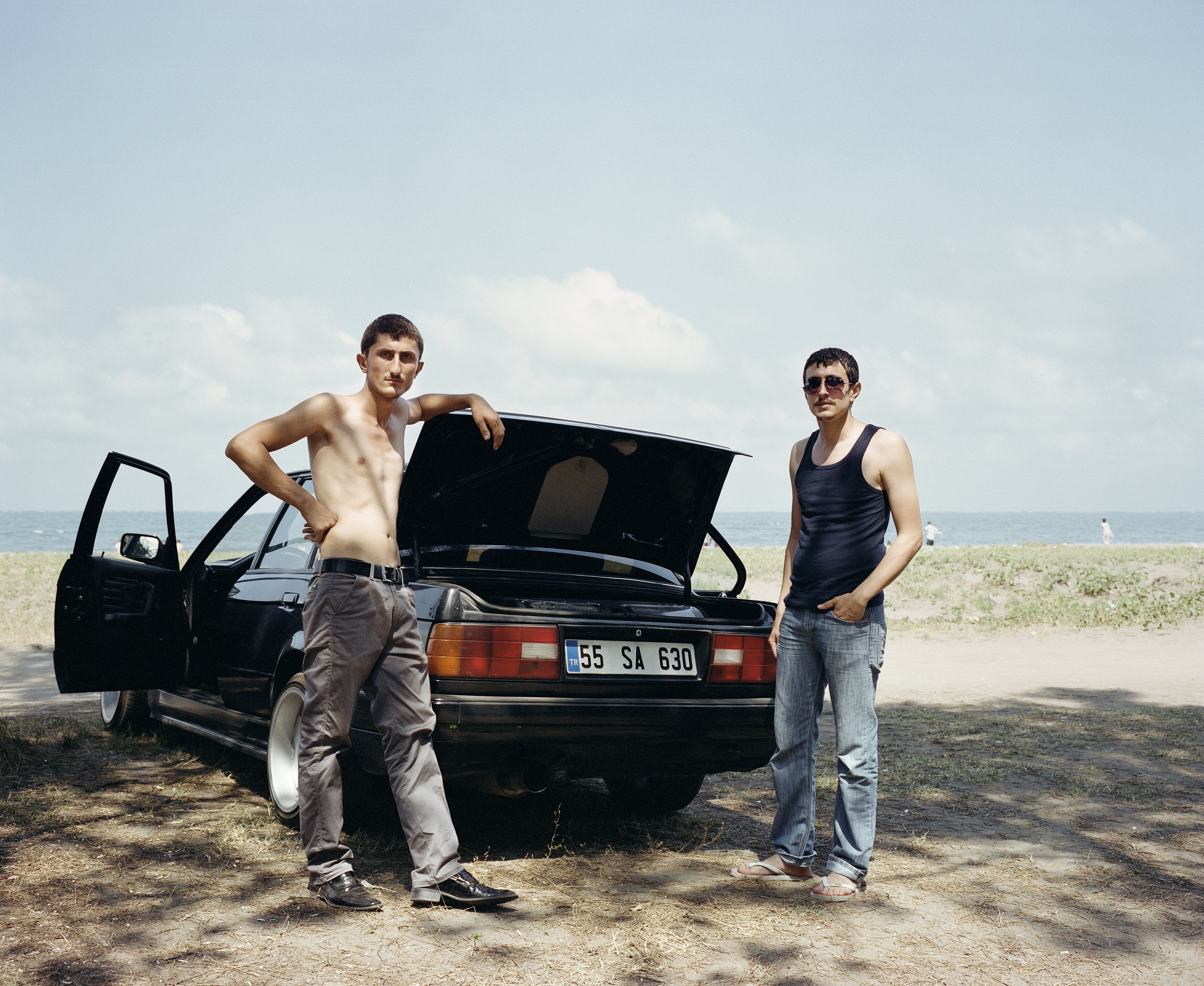 Mathias Depardon - Transanatolia. Two guys posing next to their car parked in the shade of a tree.