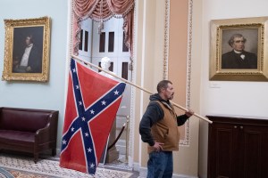 Washington DC- A protester stands with a Confederate flag after storming the Capitol during a Joint Session of Congress in which members were to certify the 2020 Presidential election.