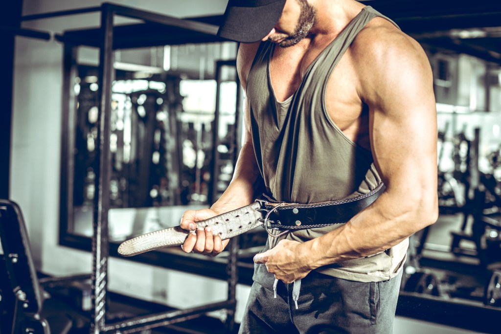 a muscular man fastening a lifting belt in a gym