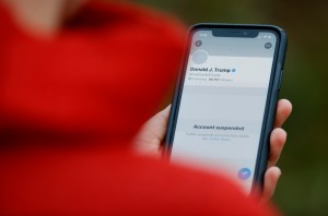 A person in a red coat holds a phone showing Donald Trump's suspended Twitter account