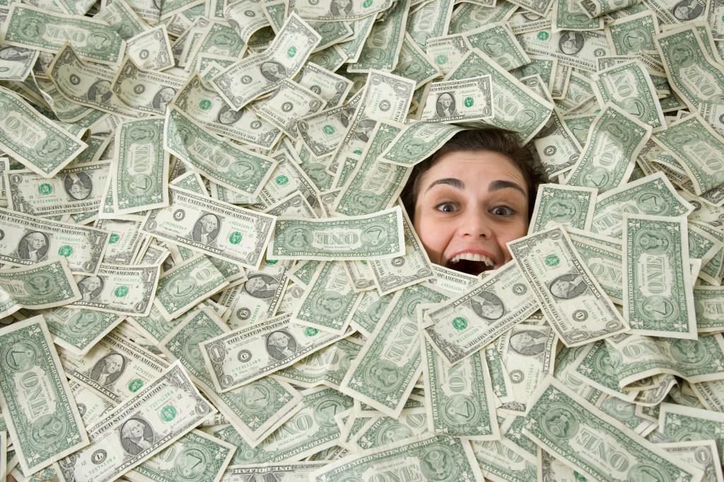 A person is smiling from under a pile of money.