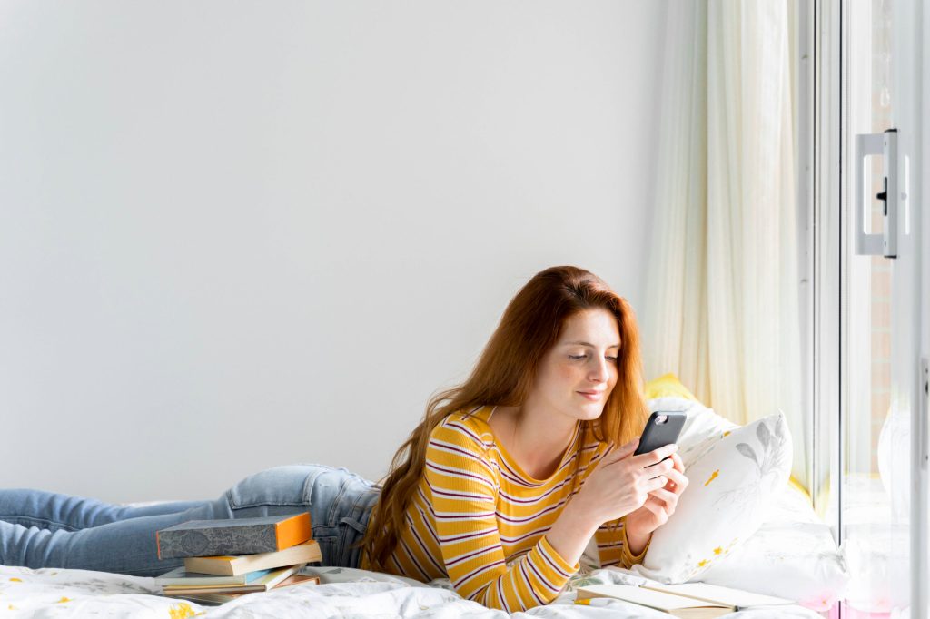 Frau liegt auf dem Bett mit Handy in der Hand, während des Lockdowns hat sich das Social Media Verhalten geändert und ich vergleiche mich weniger online