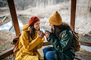 Two women relaxing in nature, in love, drinking hot drink