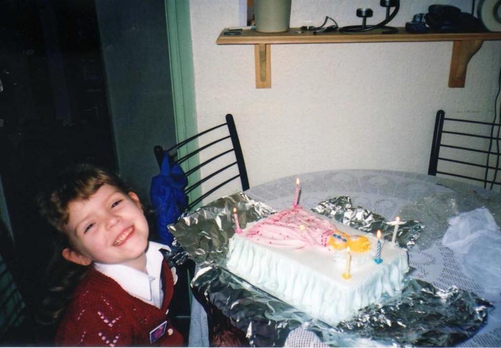 A girl standing next to a birthday cake