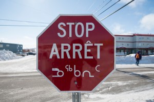 A stop sign in English, French, and Inuktitut on a snowy street in Iqaluit.