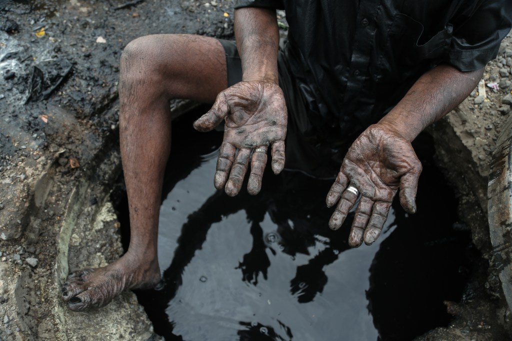 Pemulung manual menunjukkan kedua telapak tangannya yang kotor di atas kubangan hitam