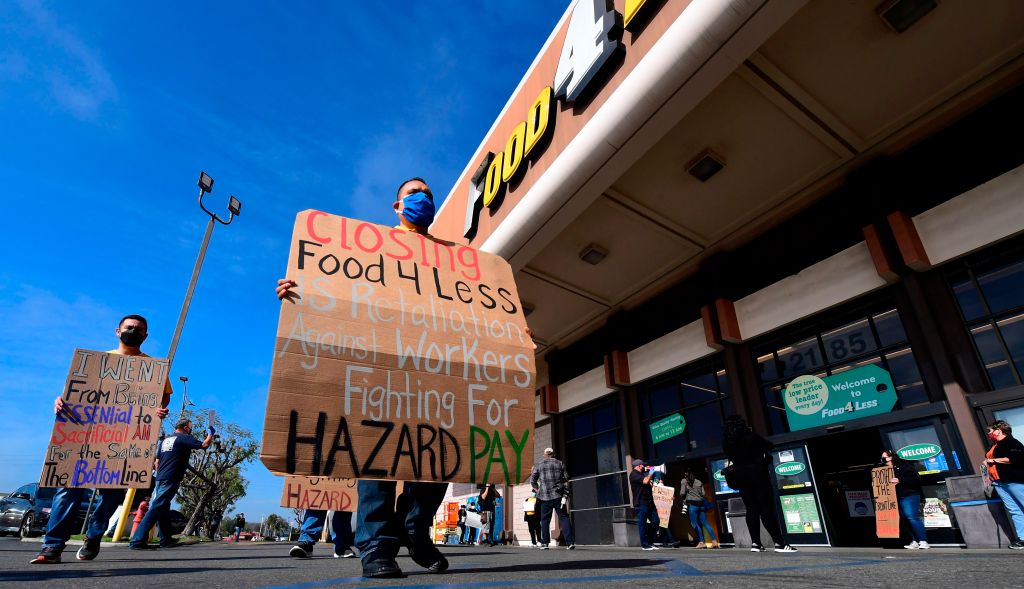 Supermarket workers hold placards in protest in front of a Food 4 Less supermarket in Long Beach, California on February 3, 2021, after a decision by owner Kroger to close two supermarkets rather than pay workers an additional $4.00 in "hazard pay" for th