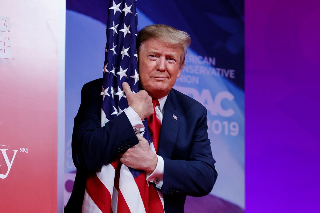 President Donald Trump hugs the American flag as he arrives to speak at the Conservative Political Action Conference, CPAC 2019, in Oxon Hill, Md., on March 2, 2019.