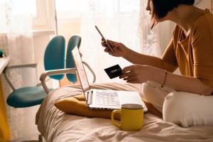 A woman sitting on a bed and onlwith a phone, a credit card, and a laptop