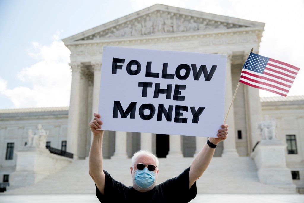 Bill Christeson holds up a sign that reads "Follow the Money" outside the Supreme Court, Thursday, July 9, 2020, in Washington.