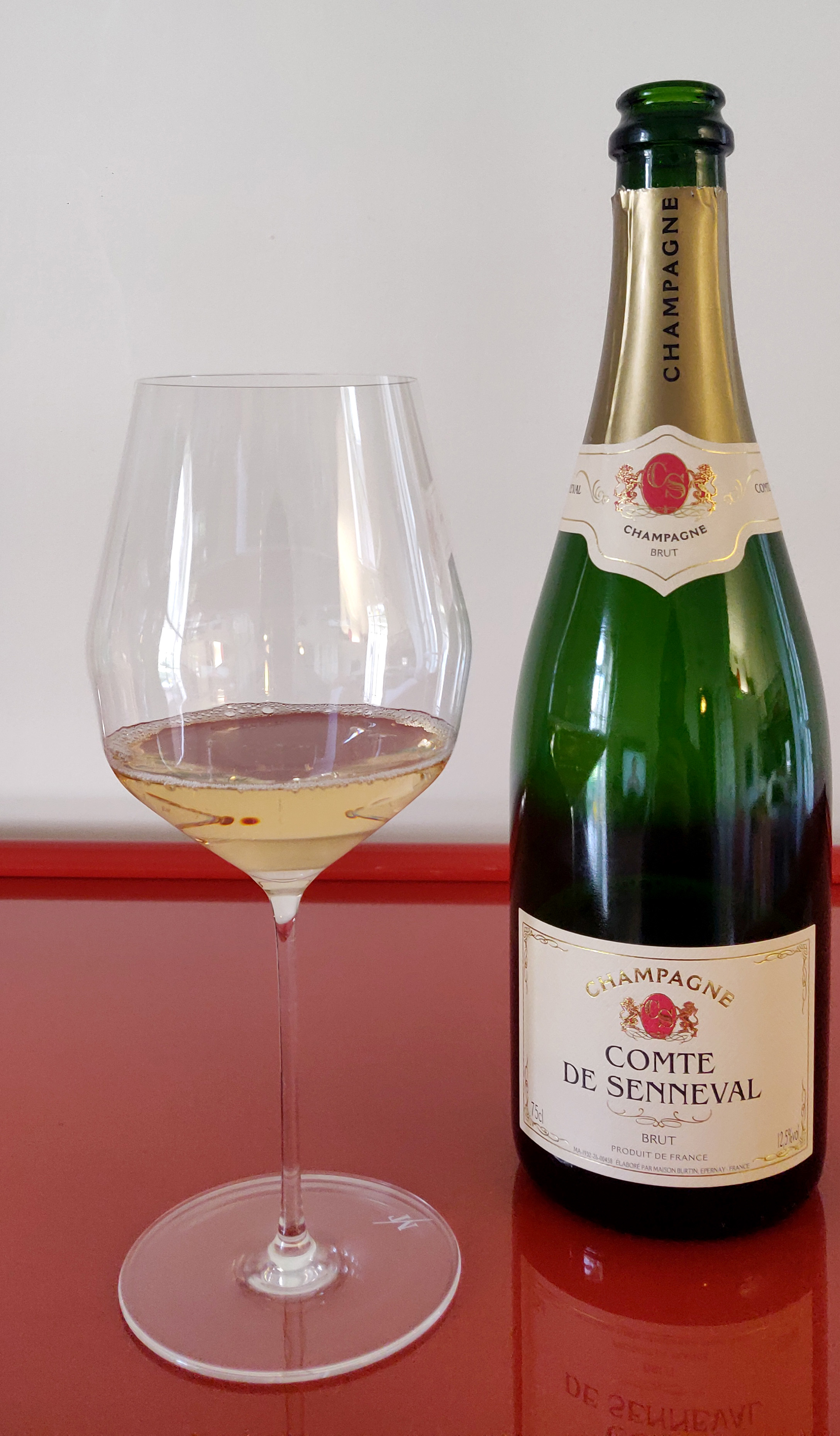 LIDL Comte de Senneval – A wine glass next to the bottle on a red glossy table.