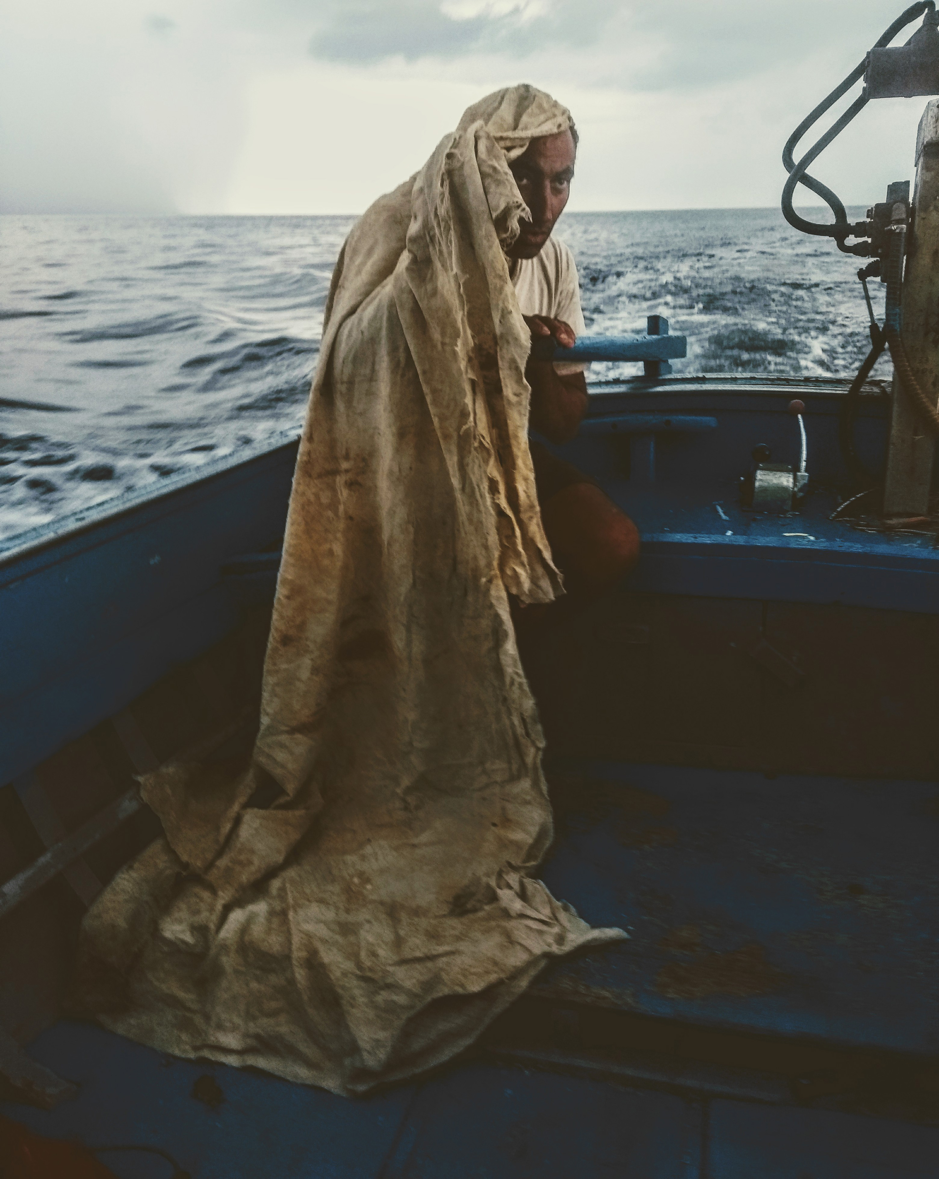 Alicudi island – a man steering a blue fishing boat with a long rag covering his head from the sun.