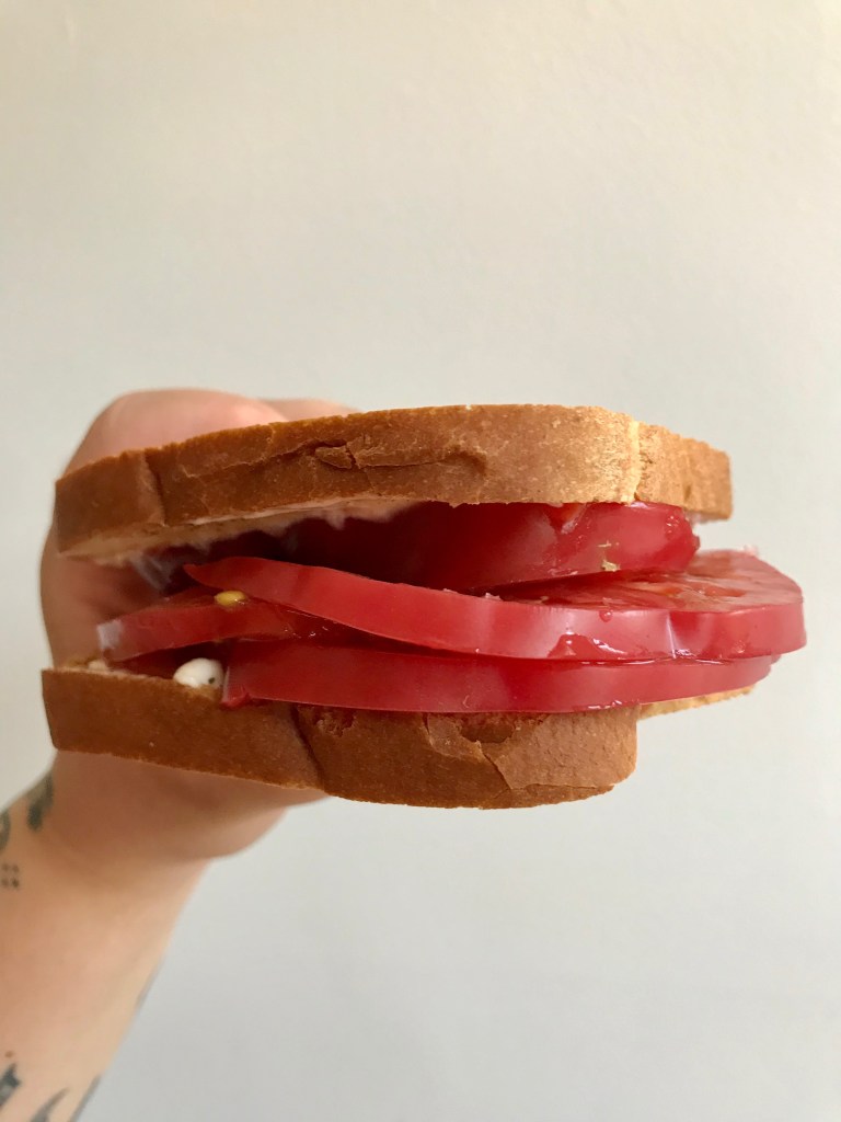 A hand holding a tomato sandwich with white bread and mayo