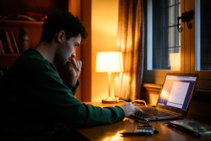 A student uses a laptop to study in a dimly-lit room.